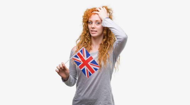 Jovem ruiva segurando bandeira do Reino Unido estressado com a mão na cabeça, chocado com vergonha e rosto surpresa, irritado e frustrado. Medo e chateado por erro
. - Foto, Imagem