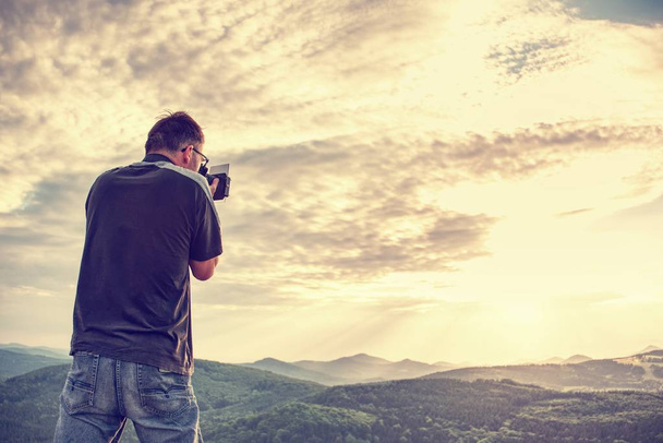 Doğa fotoğrafçısı manzara siste kirlenmiş bir dağ cliff alarak resim üzerinde. Turist ile fotoğraf makinesi ve tripod soğuk havalarda - Fotoğraf, Görsel