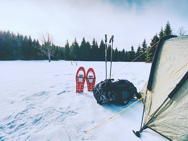 Zelt, Schneeschuhe, Trekkingstöcke und großer Rucksack bereit für einen mehrtägigen Winterausflug. Zelt im Schnee am Bergsee. - Foto, Bild