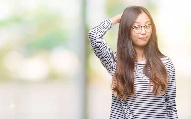 Young asian woman wearing glasses over isolated background confuse and wonder about question. Uncertain with doubt, thinking with hand on head. Pensive concept. - Fotografie, Obrázek
