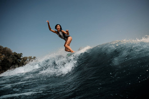 Actieve sexy brunette vrouw Wakesurfen op een bord onderaan het blauwe water op zonnige dag - Foto, afbeelding
