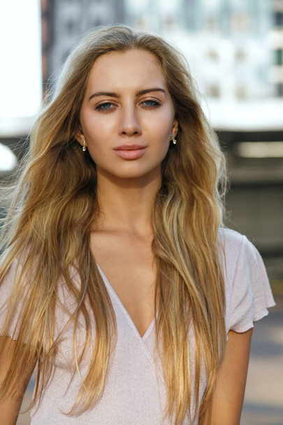Selbstbewusstes blondes Model mit perfekter Haut und langen Haaren, das auf der Straße posiert. Outdoor-Modekonzept - Foto, Bild