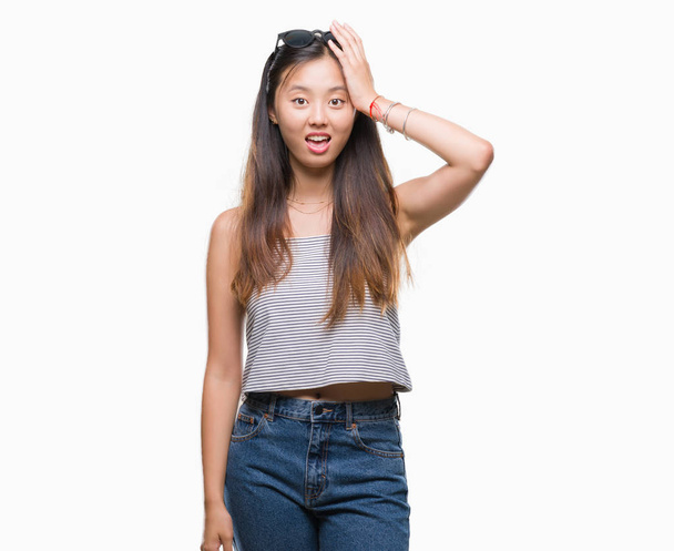 Jonge Aziatische vrouw dragen zonnebril op geïsoleerde achtergrond verrast met de hand op het hoofd voor fout, niet vergeten fout. Vergat, slecht geheugen concept. - Foto, afbeelding