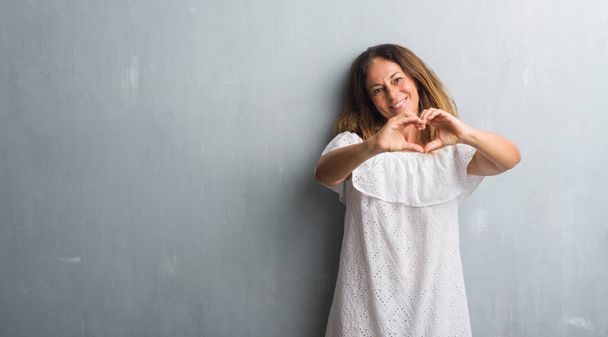 Middelbare leeftijd Latino vrouw over grijs grunge muur glimlachend in liefde met hartsymbool en vorm met de handen. Romantische concept. - Foto, afbeelding