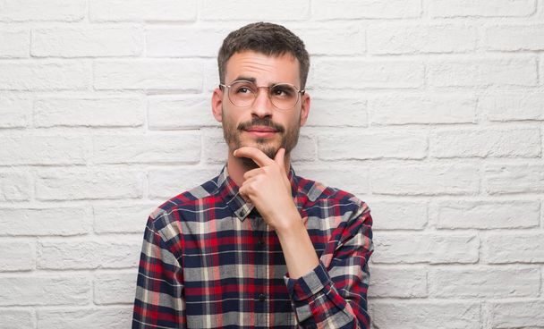 Молодой взрослый человек стоит над белой кирпичной стеной серьезное лицо, думая о вопросе, очень запутанная идея
 - Фото, изображение