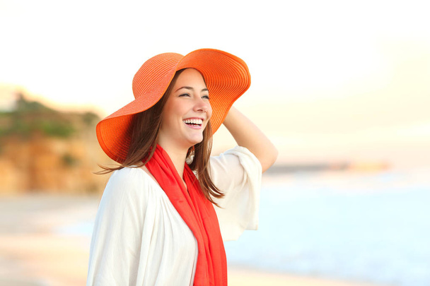 Happy woman wearing an orange picture hat contemplating ocean on the beach - Fotó, kép