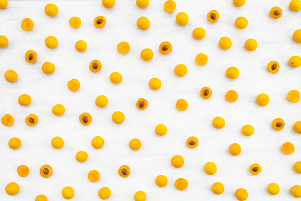 Цілі і розрізані дикі жовті сливи на білому дерев'яному фоні. Візерунок фруктів
. - Фото, зображення