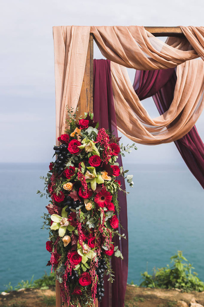 Hochzeitsbogen dekoriert mit roten Rosen, gelben Orchideen, Trauben und lila und beigen Stoffen - Foto, Bild