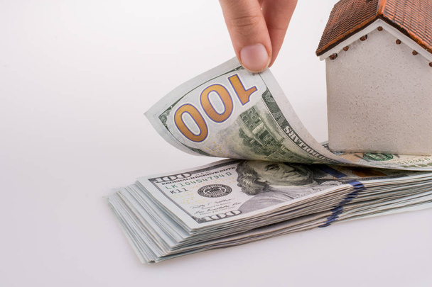 Mano humana sosteniendo billetes de dólar americano al lado de una casa modelo sobre fondo blanco
 - Foto, Imagen