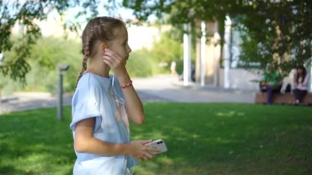Little adorable girl listening music in the park - Záběry, video