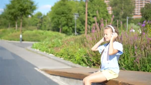 Little adorable girl listening music in the park - Materiał filmowy, wideo