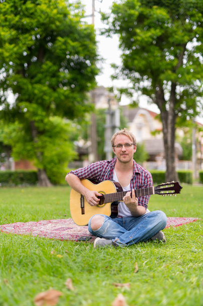 Ritratto di uomo che fa un picnic mentre suona la chitarra all'aperto
 - Foto, immagini