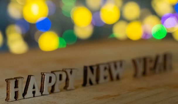 Ευτυχισμένο το νέο έτος ξύλινα γράμματα με φόντο τα φώτα bokeh. Επιλεκτική εστίαση. - Φωτογραφία, εικόνα