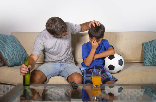 νεαρός πατέρας και ο μικρός γιος βλέποντας ποδόσφαιρο μαζί στο σπίτι καναπέ αίσθημα απογοητευμένος και λυπημένος με νίκησε την ομάδα τους χάσει το παιχνίδι στο παιδί και τον μπαμπά αποθαρρυμένος ποδόσφαιρο οπαδούς έννοια - Φωτογραφία, εικόνα