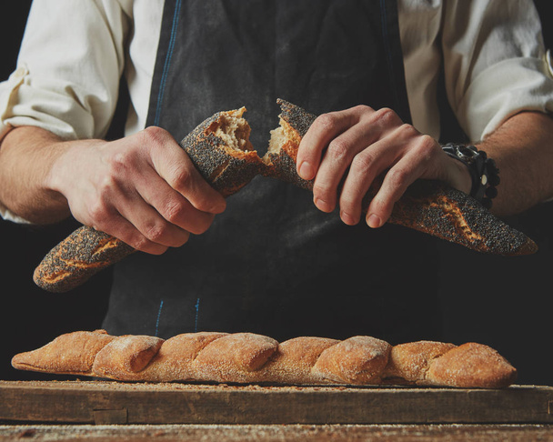 Close-up of a baker man holding fresh halves of a baguette with a poppy - Photo, Image