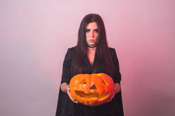 Готическая молодая женщина в костюме ведьмы на Хэллоуин с резной тыквой
 - Фото, изображение