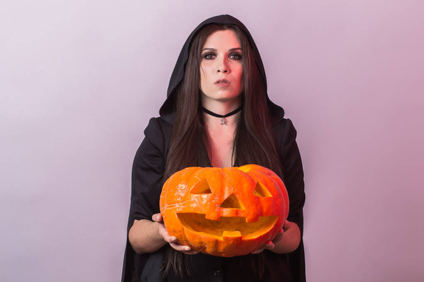 Young woman in Halloween witch costume in studio with yellow pumpkin. - Photo, Image