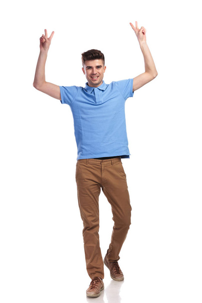 glücklicher junger, lässiger Mann, der den Erfolg mit den Händen in der Luft feiert und das Siegeszeichen auf weißem Hintergrund macht - Foto, Bild