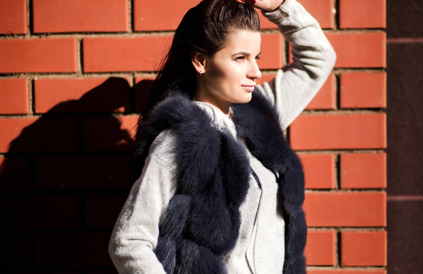 photo of girl in a fur vest against a brick wall background - 写真・画像
