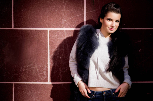 photo of girl in a fur vest against a brick wall background - Фото, зображення