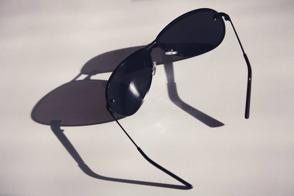 Dark sunglasses lie on a white table, with long shadows, concept fashion - Photo, Image