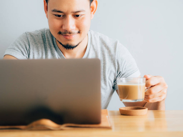 Happy asian man drink coffee while use laptop. - Zdjęcie, obraz