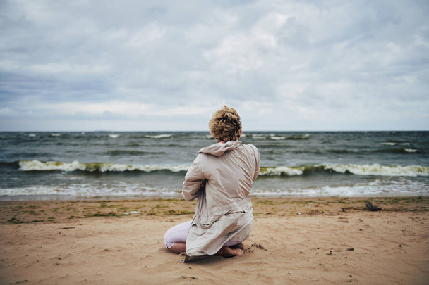 anonyme Frau in Jacke blickt aufs Meer - Foto, Bild