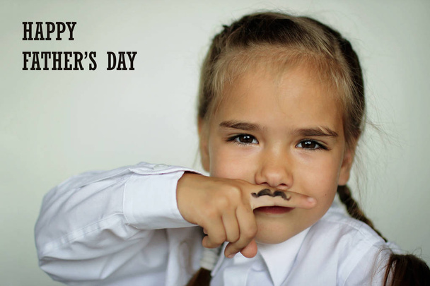 A cute little girl holding a finger in front of her face with drawn fake moustache on it, happy father day and men health concept - Photo, Image
