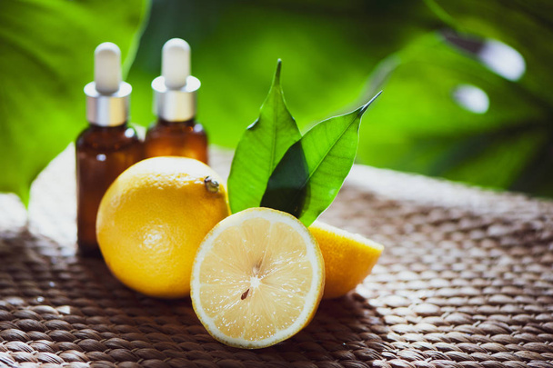 Flessen met citroenolie, vers fruit geheel en de helft op een natuurlijke tropische achtergrond. - Foto, afbeelding