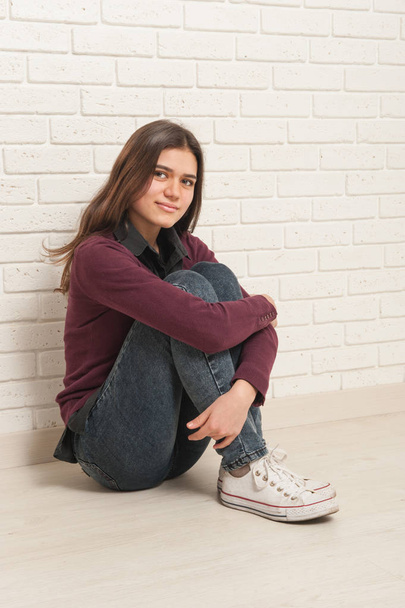 girl sitting on the floor against a brick wall - Foto, Imagen