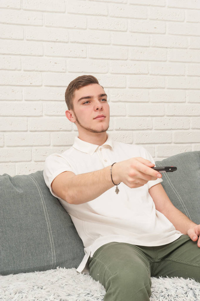 A teenager with a remote control sits on the couch and watches TV - Fotografie, Obrázek