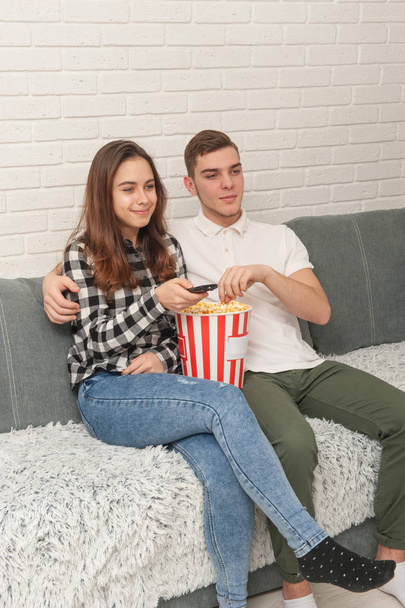 Two teenagers are sitting on the couch watching TV - Foto, afbeelding