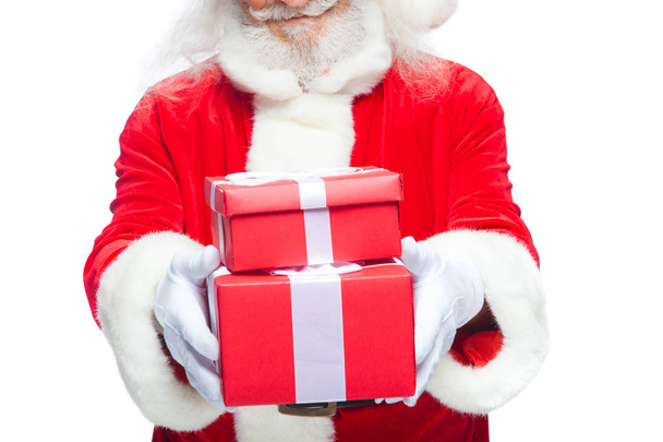 Kerstmis. Glimlachend Santa Claus in witte handschoenen houdt twee rode geschenkverpakkingen met een boog, een op de andere. Geïsoleerd op een witte achtergrond. Close-up - Foto, afbeelding