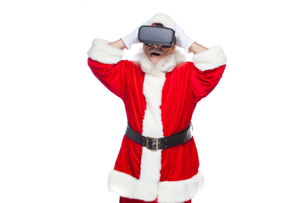 Christmas. Santa Claus in black virtual reality glasses makes gestures with his hands. Surprise, emotion. New technology. Isolated on white background. - Foto, imagen