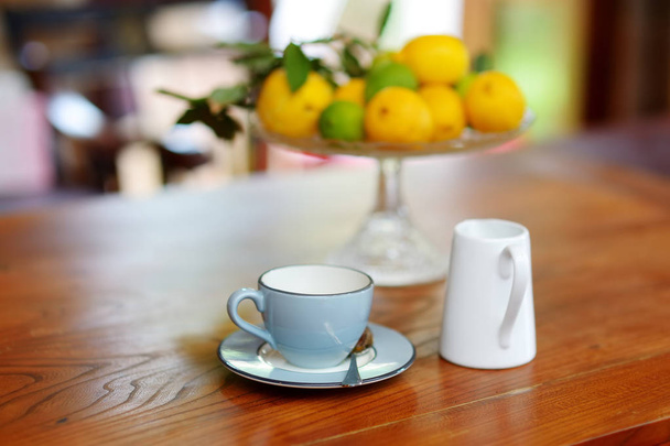Beautiful blue ceramic tea-cup on a wooden table, with a dish of ripe lemons on the background. - Foto, Imagen