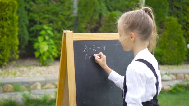 Gelukkig weinig schoolmeisje met een krijtbord buiten - Video