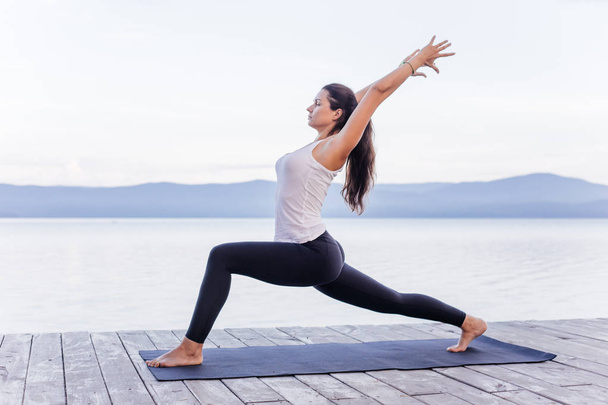 Young attractive smiling woman practicing yoga on a lake - Foto, Imagen