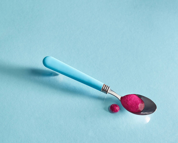 Natural smoothies of red berries in a spoon on a glass blue background and cocktail drop on the surface with soft shadows and reflection. - Foto, imagen