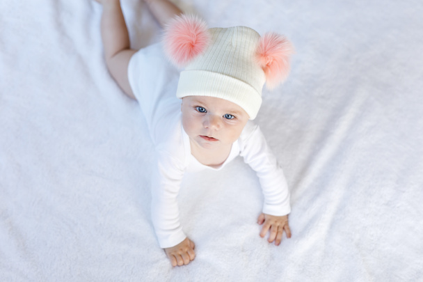 Симпатичный обожаемый ребенок в теплой белой и розовой шляпе с симпатичными сапогами. Счастливая девочка учится ползать и смотреть в камеру. Крупный план на рождественский праздник и семейную концепцию - Фото, изображение