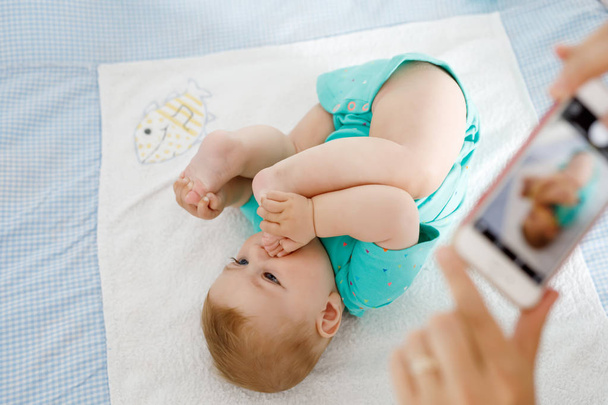 Parent taking photo of a baby with smartphone. Adorable newborn child taking foot in mouth. sucking feet. Digital family memories. - Photo, image