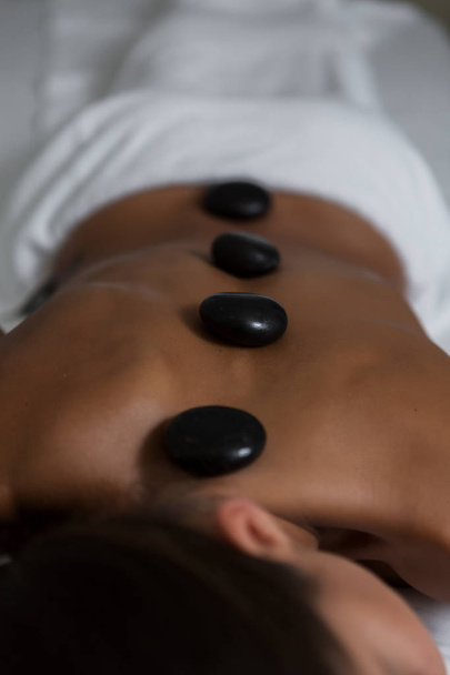 Foto aerea di donna anonima sdraiata nuda sul tavolo con poche pietre calde nere sul retro godendo di un massaggio nel salone SPA
  - Foto, immagini