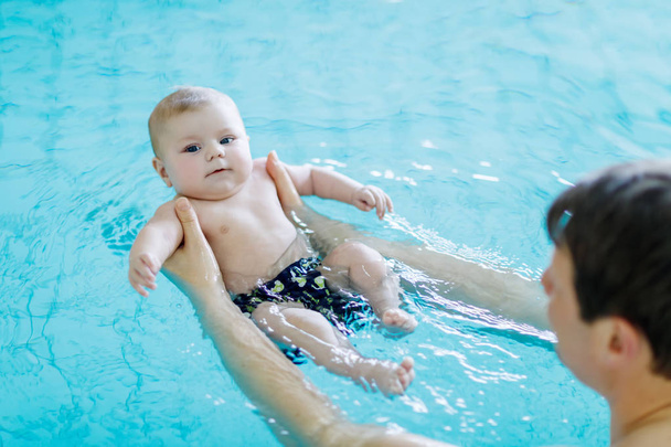 Happy middle-aged father swimming with cute adorable baby in swimming pool. Smiling dad and little child, newborn girl having fun together. Active family spending leisure and time in spa hotel - Foto, Imagem