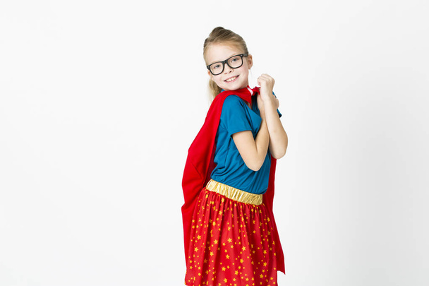 blond supergirl with glasses and red robe und blue shirt is posing in the studio - Foto, Bild