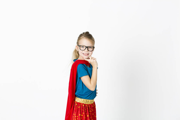 blond supergirl with glasses and red robe und blue shirt is posing in the studio - Foto, Bild