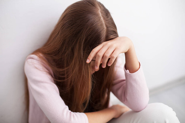 Depression in adolescence - young teenager girl sitting by the wall propping her head overwhelmed by problems - Photo, Image