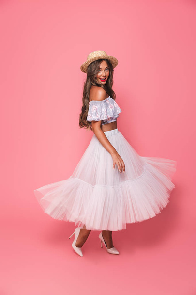 Full length portrait of adorable fashion woman 20s wearing straw hat and fluffy skirt smiling and looking at you isolated over pink background in studio - Fotó, kép