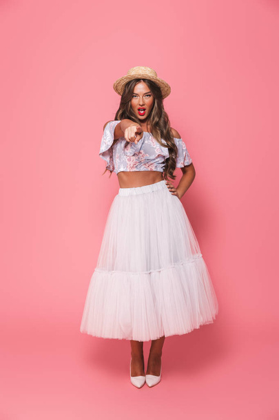 Full length portrait of beautiful fashion woman 20s wearing straw hat and fluffy skirt pointing finger forward at you isolated over pink background in studio - Foto, immagini