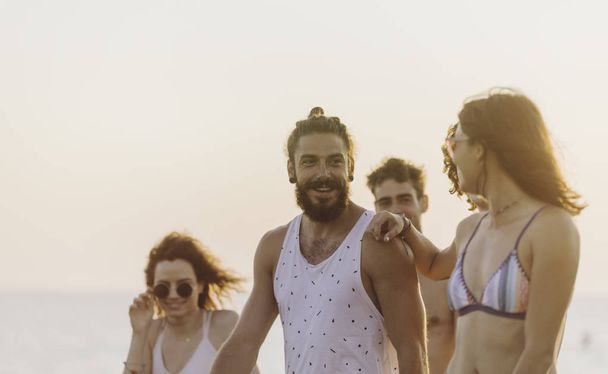 Group of young men and women walking on sandy beach and looking happy. - 写真・画像
