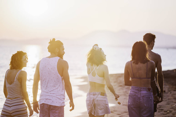 Gruppe junger Männer und Frauen spaziert am Sandstrand und sieht glücklich aus. - Foto, Bild