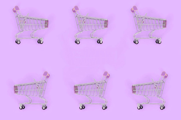 Einkaufssucht, Shopping-Liebhaber oder Shopaholic-Konzept. viele kleine leere Einkaufswagen führen ein Muster auf pastellfarbenem Papierhintergrund aus. flache Verlegekomposition, Ansicht von oben - Foto, Bild